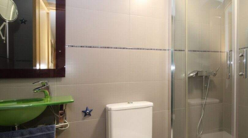 Modern bathroom of the ground floor apartment in Palma with green sink, glass shower and beige wall tiles.