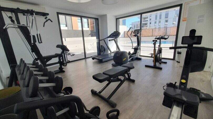 Moderner Fitnessraum mit Geräten und Panoramafenster mit Poolblick im Penthouse Nou Llevant, Palma