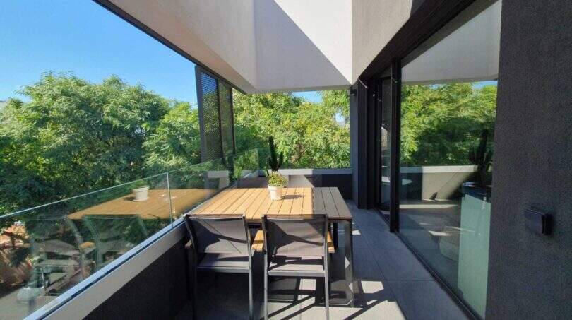 Moderne Dachterrasse des Penthouses in Nou Llevant mit Esstisch, Glasgeländer und Blick ins Grüne.