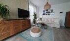 Helles Wohnzimmer des Penthouses mit weißem Sofa, Holzmöbeln, türkisem Teppich und mediterranem Flair.