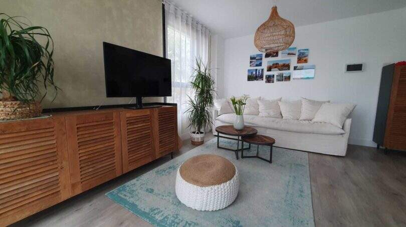 Helles Wohnzimmer des Penthouses mit weißem Sofa, Holzmöbeln, türkisem Teppich und mediterranem Flair.