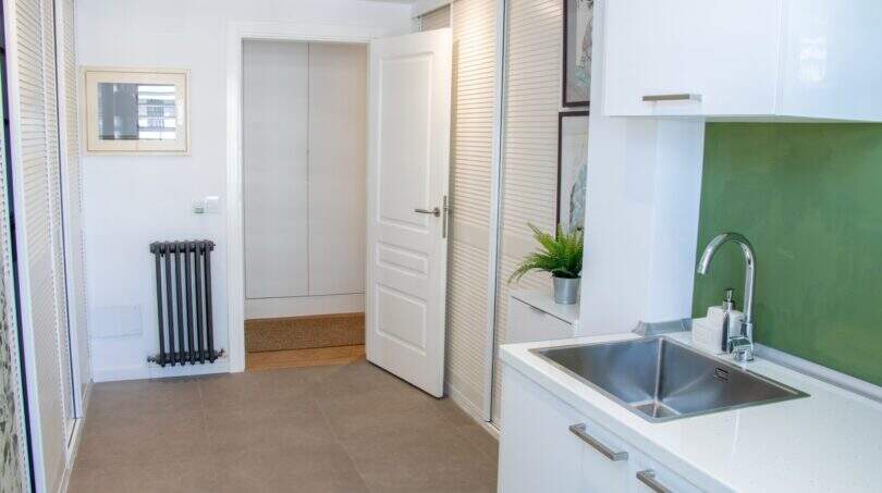 Helle Küche mit weißen Schränken, grüner Rückwand, Edelstahlspüle und Blick zur Eingangstür in Designerwohnung Palma