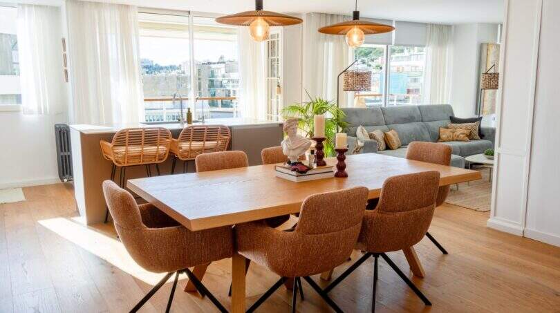 Bright living-dining room with wooden table, rattan chairs and view of Palma's cityscape