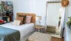 Helles Schlafzimmer der Designerwohnung in Palma mit Rattanbett, grüner Tagesdecke, großem Spiegel und Bücherregal
