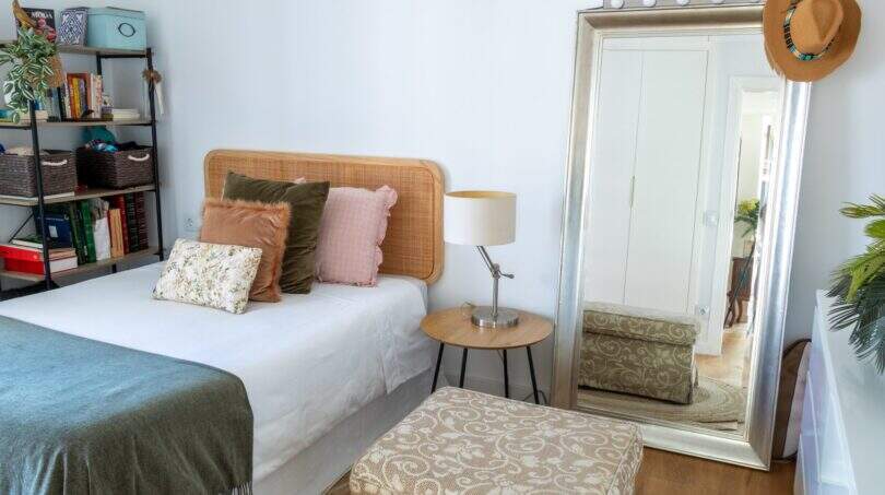 Helles Schlafzimmer der Designerwohnung in Palma mit Rattanbett, grüner Tagesdecke, großem Spiegel und Bücherregal