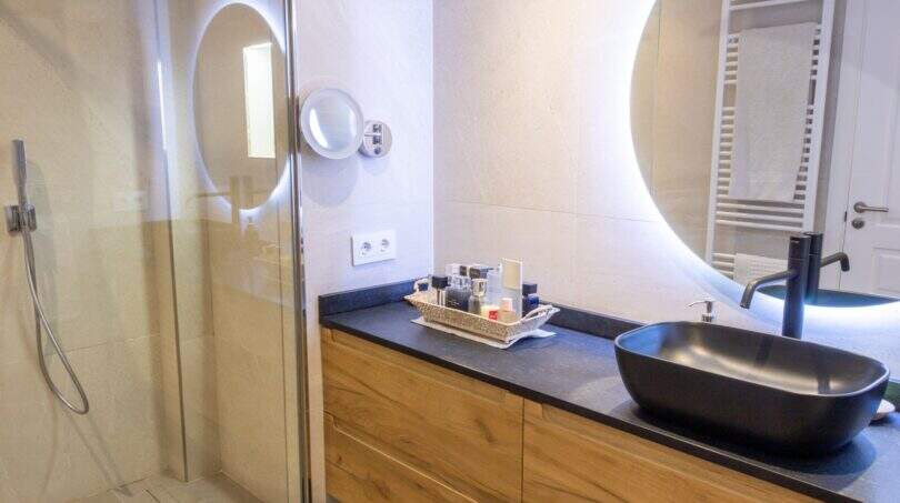 Modernes Badezimmer der Designerwohnung in Palma mit schwarzem Aufsatzbecken, Holzunterschrank und beleuchtetem Rundspiegel.