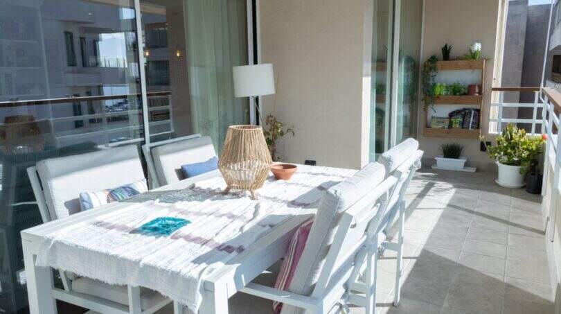 Sonnige Dachterrasse mit weißem Gartentisch, Stühlen und Pflanzenregal der Designerwohnung am Paseo Maritimo