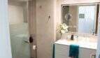 Modernes Badezimmer der Designerwohnung in Palma mit Glasdusche, weißem Waschtisch und dekorativen Blumen
