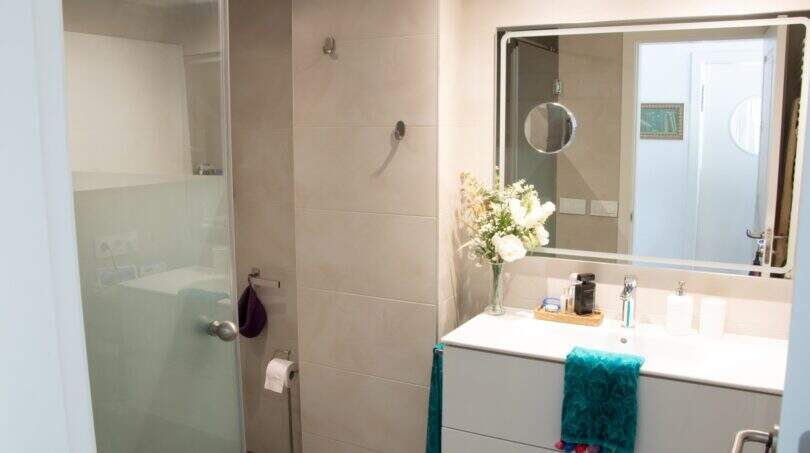 Modernes Badezimmer der Designerwohnung in Palma mit Glasdusche, weißem Waschtisch und dekorativen Blumen