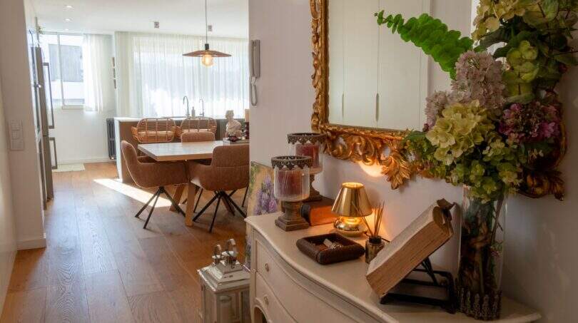 Eleganter Eingangsbereich der Designerwohnung mit vergoldetem Spiegel, weißer Kommode und Blick ins lichtdurchflutete Esszimmer