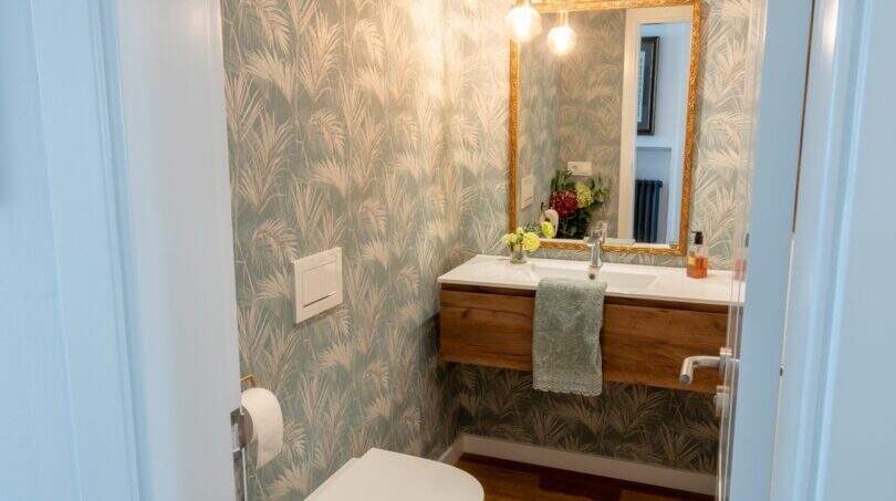 Elegantes Gäste-WC mit Tropenprint-Tapete, vergoldetem Spiegel und Holzwaschtisch in Designerwohnung Palma