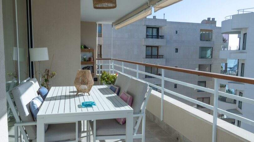 Sonnige Dachterrasse mit weißem Esstisch, Rattanleuchte und Glasgeländer in Designerwohnung am Paseo Maritimo