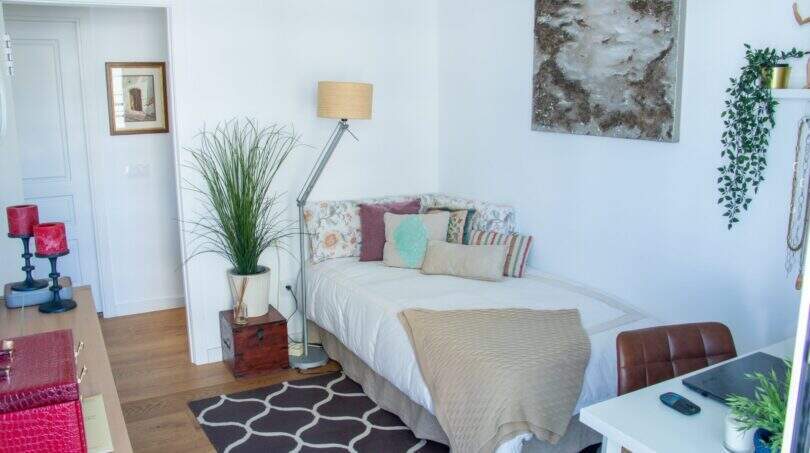 Helles Schlafzimmer mit Einzelbett, bunten Kissen, Stehlampe, Zimmerpflanze und moderner Wandkunst in Palma-Wohnung