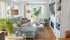 Helles Wohnzimmer mit grauem Ecksofa, Einbauregal, Kamin und großen Fenstern mit Stadtblick