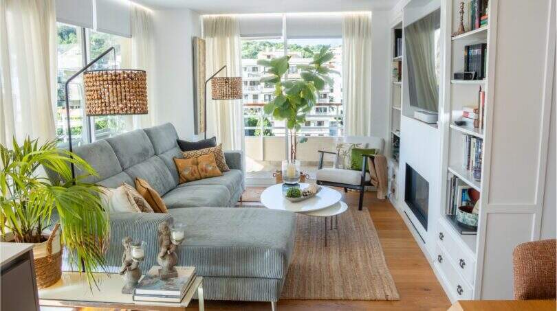 Helles Wohnzimmer mit grauem Ecksofa, Einbauregal, Kamin und großen Fenstern mit Stadtblick