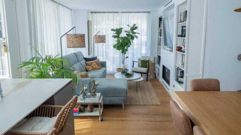 Helles Wohnzimmer mit grauem Sofa, Einbauregal, Parkett und großen Fenstern in Designerwohnung Palma