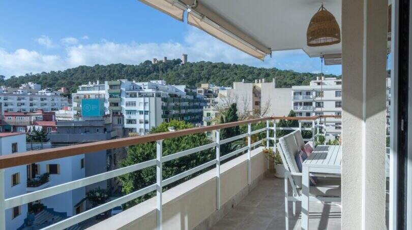 Heller Balkon mit weißem Geländer, Sitzgruppe und Blick auf Palmas Stadtpanorama mit bewaldeter Anhöhe