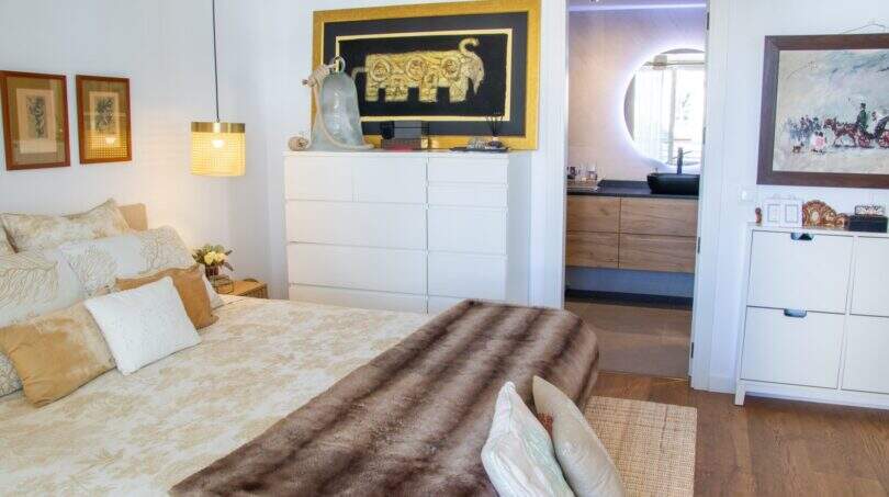 Elegantes Schlafzimmer der Designerwohnung in Palma mit Doppelbett, Pelzdecke, weißen Kommoden und En-suite-Bad.