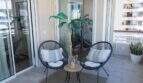 Sonnige Terrasse der Designerwohnung in Palma mit zwei Korbstühlen, Beistelltisch und tropischer Pflanze