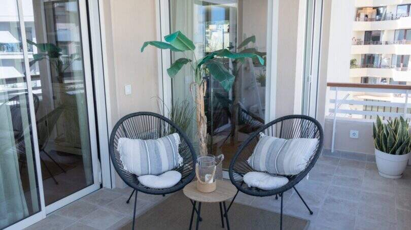 Sonnige Terrasse der Designerwohnung in Palma mit zwei Korbstühlen, Beistelltisch und tropischer Pflanze