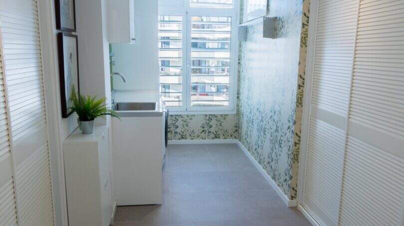 Heller Hauswirtschaftsraum mit floralem Tapetenmuster, weißen Einbauschränken und Fenster in Designerwohnung am Paseo Maritimo