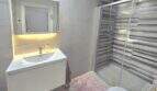 Modern bathroom with illuminated mirror, white sink and glass shower in Palmanova apartment