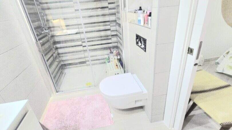 Modern bathroom of the Meereslinie apartment in Palmanova with shower, wall-mounted toilet and pink bath mat