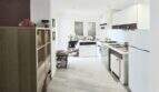 Bright kitchen of the Meereslinie apartment in Palmanova with white cabinets, wooden floor and modern shelving.