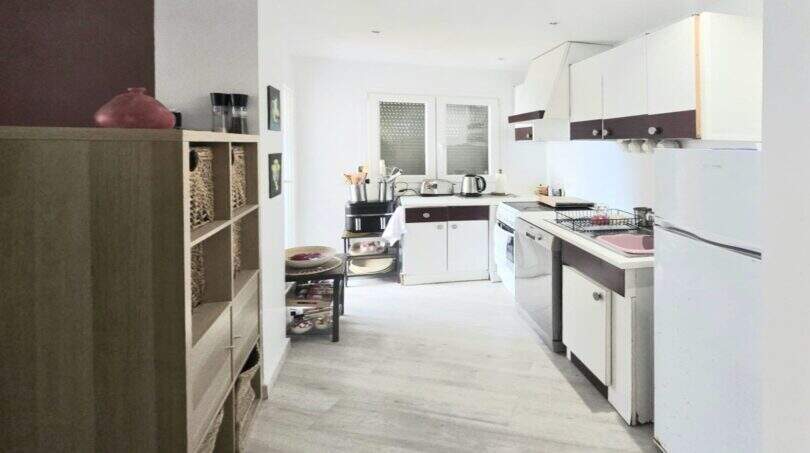 Bright kitchen of the Meereslinie apartment in Palmanova with white cabinets, wooden floor and modern shelving.