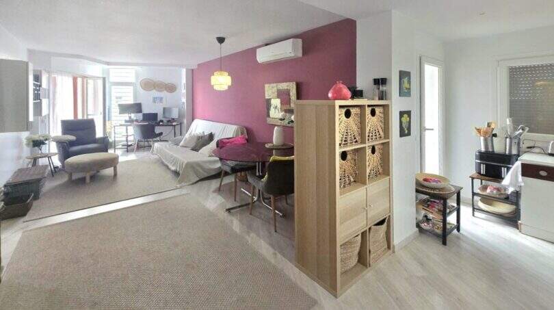 Bright living room with kitchen area, room divider, air conditioning and magenta accent wall in Palmanova apartment.
