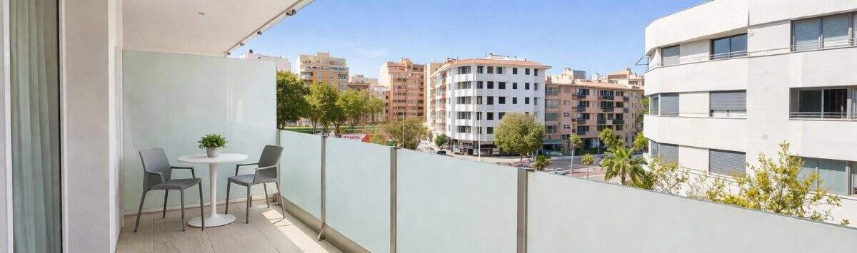 Sonniger Balkon mit Glasgeländer, Tisch und Stühlen, Blick auf Palmas Stadtbild und blauer Himmel