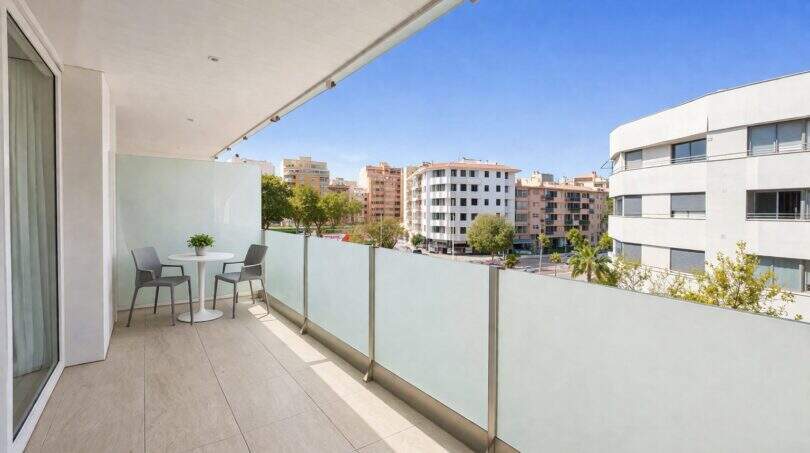 Sonniger Balkon mit Glasgeländer, Tisch und Stühlen, Blick auf Palmas Stadtbild und blauer Himmel