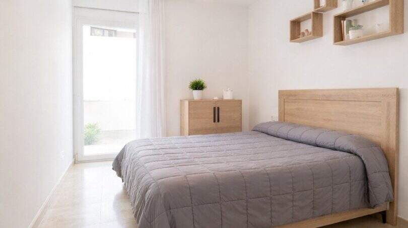 Helles Schlafzimmer mit Doppelbett, Holzmöbeln, Wandregalen und Zugang zum Balkon in Palma