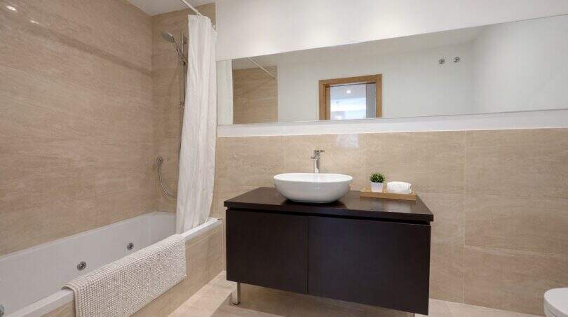 Modernes Badezimmer mit Whirlpool-Badewanne, dunklem Waschtisch und beigen Fliesen in Palma-Apartment