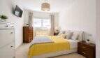 Helles Schlafzimmer mit Doppelbett, gelbem Überwurf, Holzmöbeln und TV in Palma de Mallorca