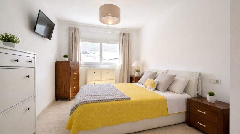 Helles Schlafzimmer mit Doppelbett, gelbem Überwurf, Holzmöbeln und TV in Palma de Mallorca