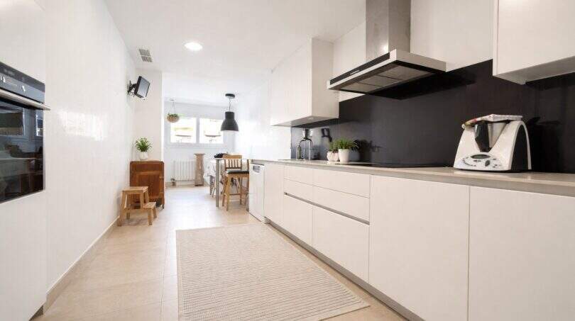 Moderne weiße Einbauküche mit schwarzer Rückwand, Dunstabzug und Esstisch in Palma de Mallorca