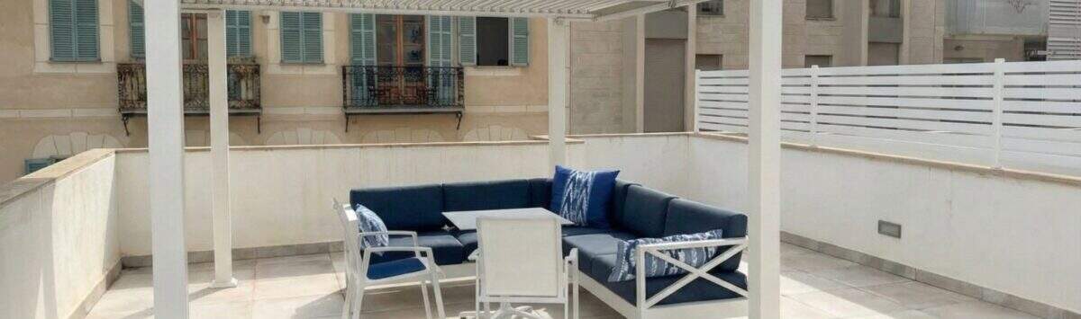 Soleada terraza en la azotea con pérgola blanca, mobiliario lounge azul y vistas a la ciudad en Palma de Mallorca