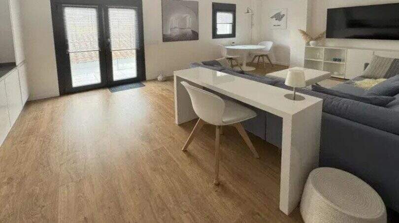 Helles Wohnzimmer mit Holzboden, grauem Sofa, weißem Schreibtisch und Terrassenzugang im Penthouse Palma