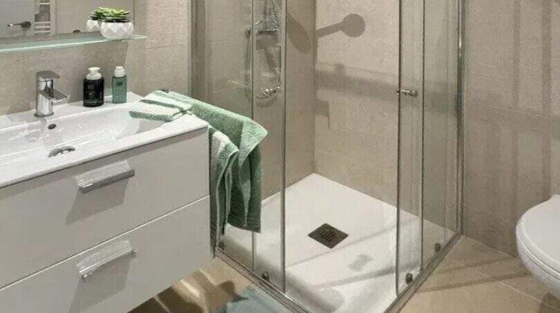 Modernes Badezimmer des Penthouses mit Glasdusche, weißem Waschtisch und mintgrünen Akzenten in Palma