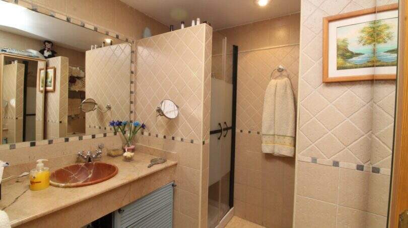 Elegant bathroom with marble sink, beige tile cladding, shower and wall mural in Palma de Mallorca