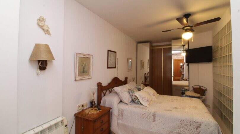 Bedroom with double bed, wooden furniture, ceiling fan and glass block wall in Palma de Mallorca