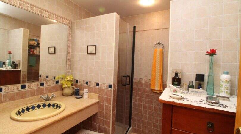 Bright bathroom with shower, beige tiles, decorative sink and wooden dresser in Palma de Mallorca.