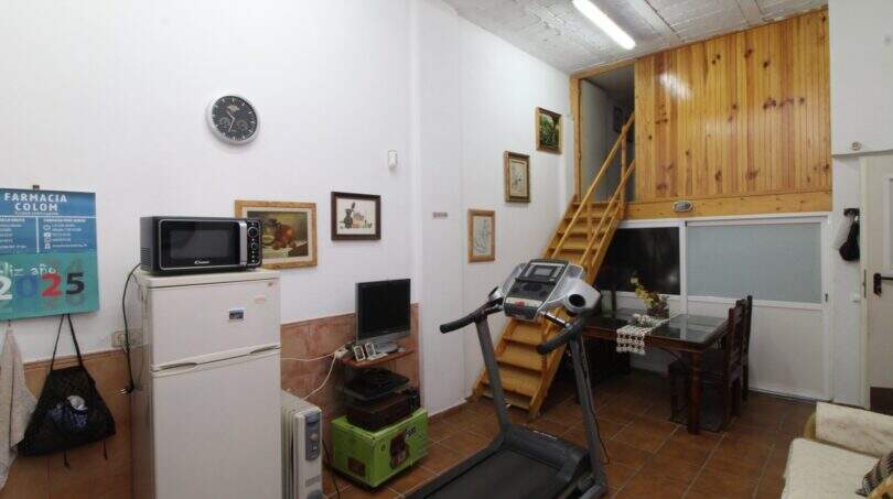 Multi-purpose room with treadmill, refrigerator, microwave and wooden staircase to upper floor in Palma
