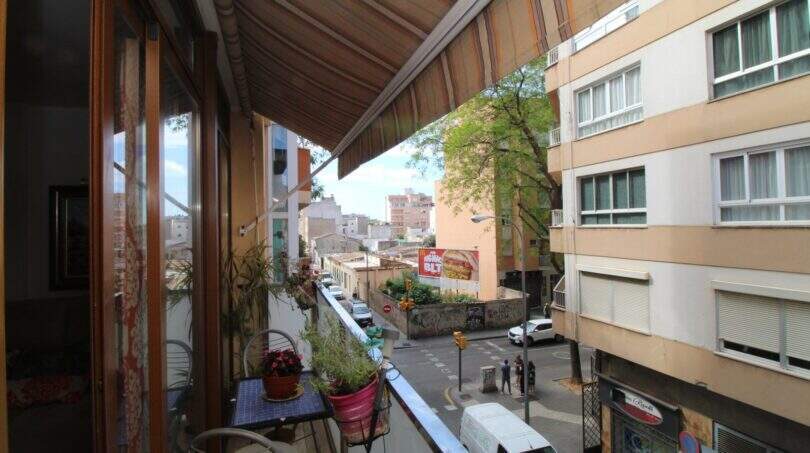 Balcony with awning, plants and city view of Palma de Mallorca, multi-story residential buildings in the background