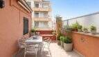 Sunny roof terrace with dining table, chairs and potted plants, view of neighboring buildings in Palma de Mallorca.