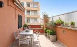 Sonnige Dachterrasse mit Esstisch, Stühlen und Topfpflanzen, Blick auf Nachbargebäude in Palma de Mallorca.