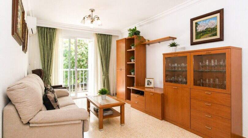 Helles Wohnzimmer der Wohnung in Portixol mit Holzmöbeln, Sofa, Vitrine und Balkon mit Grünblick.