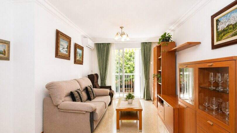 Helles Wohnzimmer der Wohnung in Portixol mit Sofa, Holzvitrine und Balkon mit Grünblick.