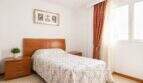 Schlafzimmer der Wohnung in Portixol mit Doppelbett, Holzmöbeln und roten Vorhängen am Fenster.